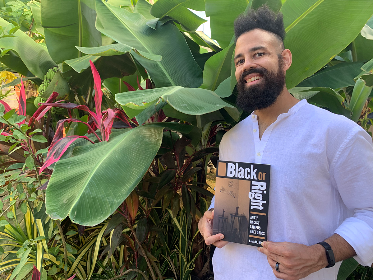 Dr. Louis Maraj poses with his book in front of tropical plants