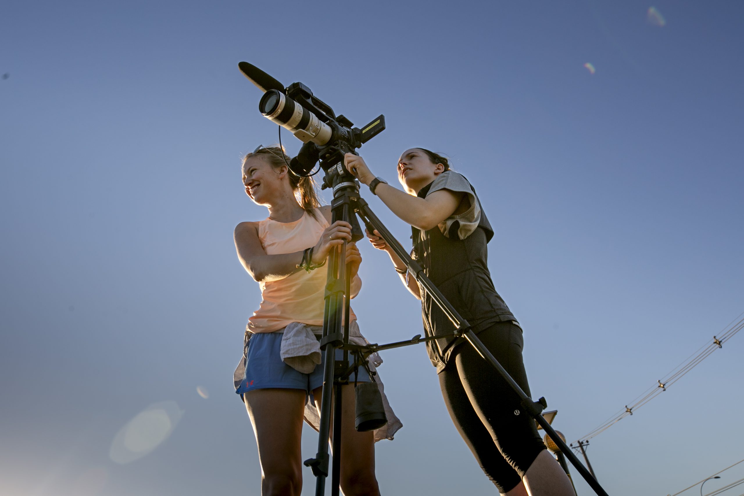 Two UBC Journalism students setting up a video camera against a blue sky.