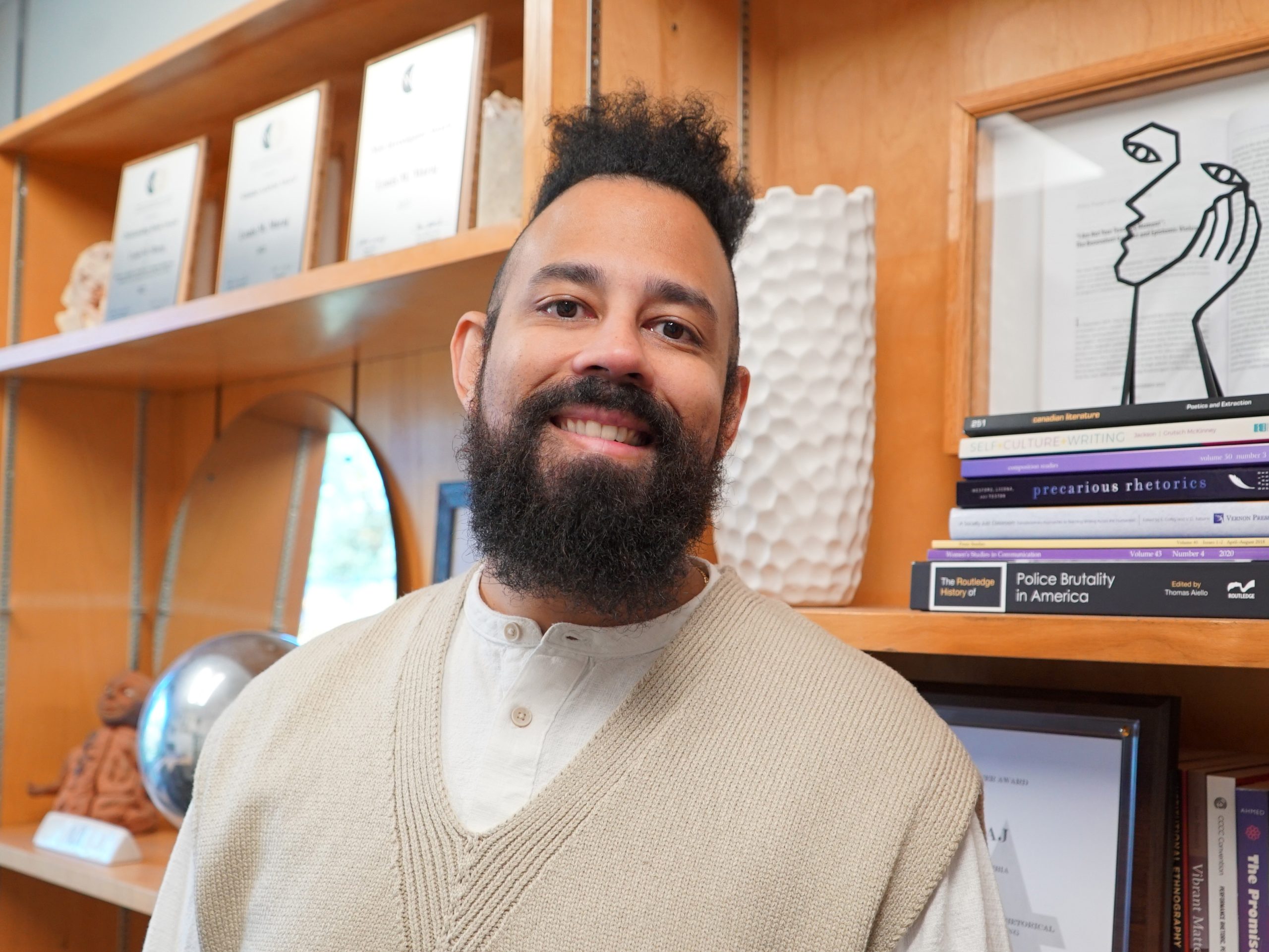 Dr. Maraj standing in his office in front of a book shelf full of books, awards, and certificates.