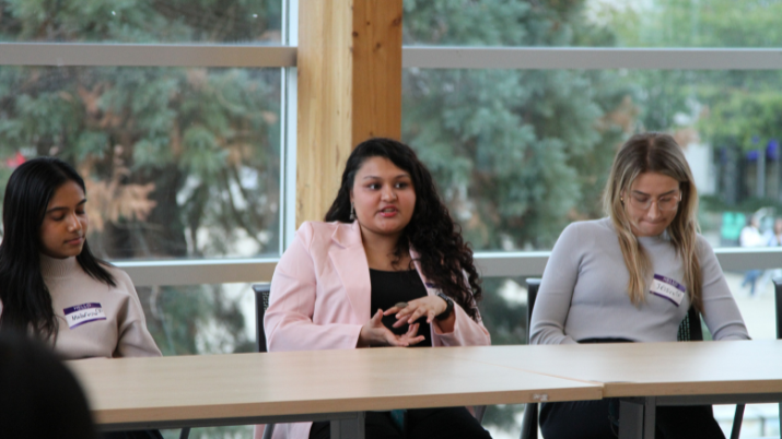 A woman wearing a pink jacket talking at a conference panel